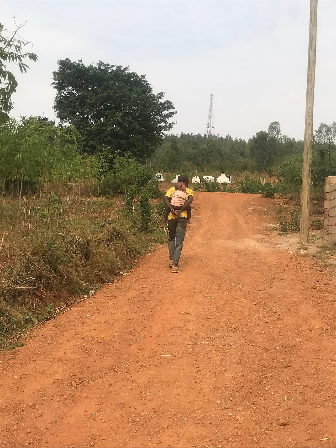 A man carrying a child in his arms along a red-dirt road