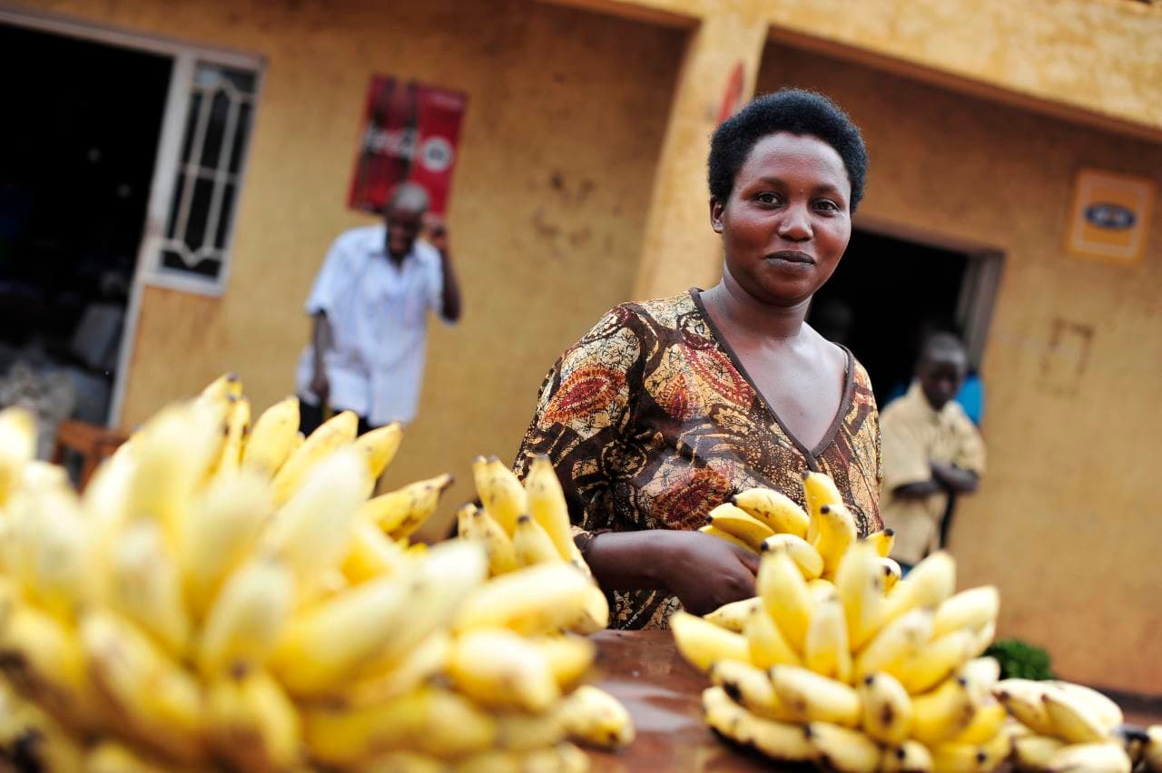 A woman at a market stall stacked with fresh bananas